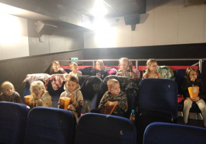 Dzieci częstują się popcornem przed rozpoczęciem seansu filmowego